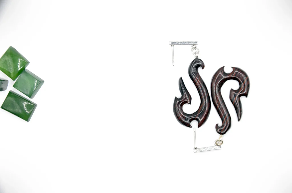 Boucles d’oreilles artisanales en bois brun sculpté avec un motif « Hei Matau » d’inspiration maorie.