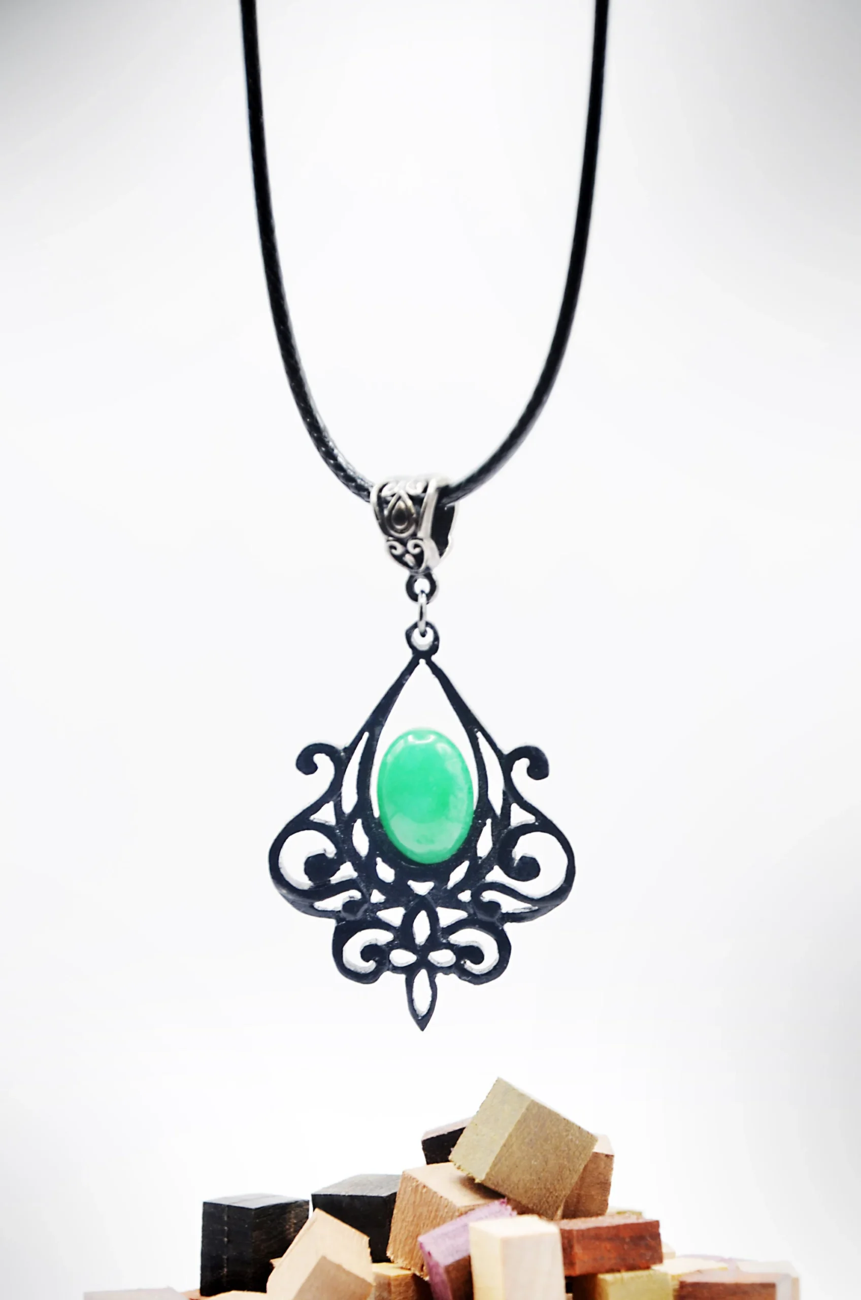 Collier artisanal en bois d’ébène noir sculpté avec des motifs végétaux entrelacés, associé à une pierre de jade vert.