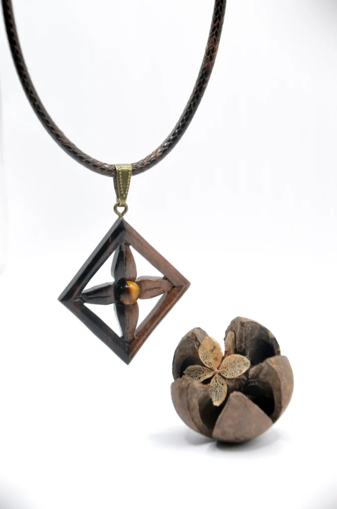 Collier artisanal en bois d’ébène bicolore sculpté avec un motif de fleurs à quatre pétales d’inspiration néolithique, associé à une pierre d’œil de tigre.