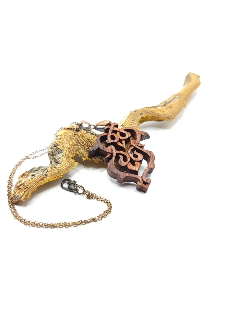Collier artisanal en bois de palissandre sculpté avec un motif de médaillon, posé contre une branche de bois.