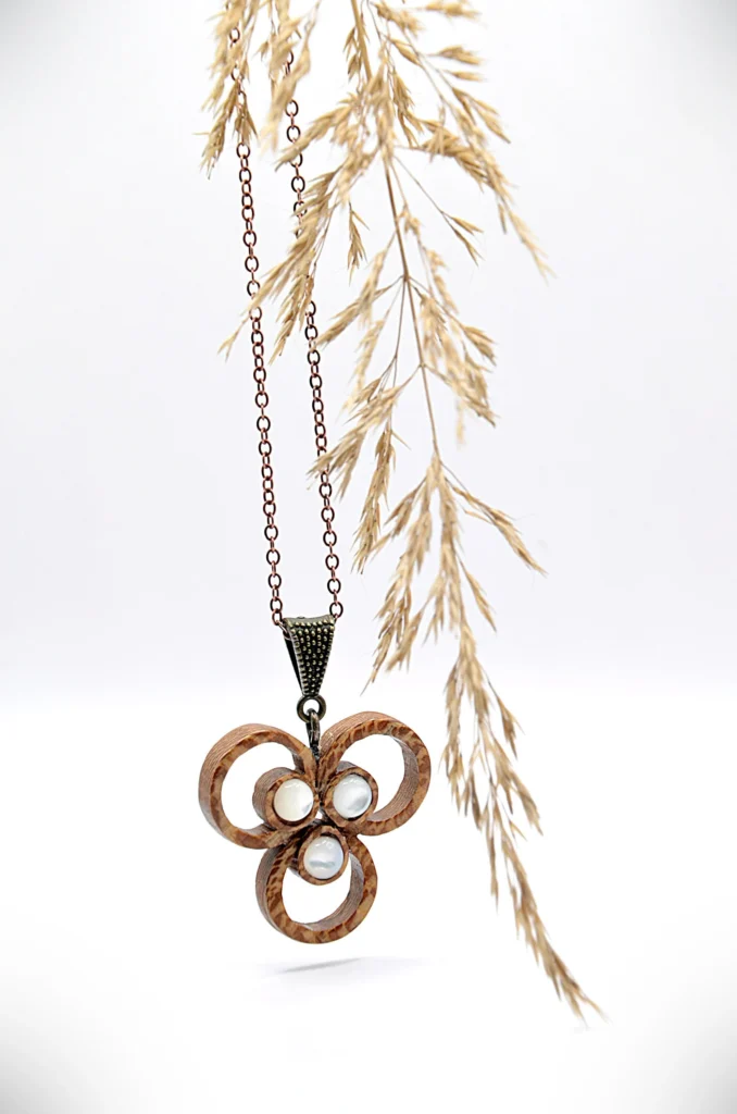 Collier artisanal en bois de platane moucheté avec un motif de trois anneaux entrelacés, accompagné d’un élément en nacre.