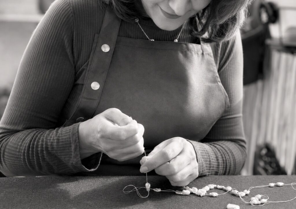 Artisane MANANTIQUE enfilant à la main des perles naturelles dans son atelier.